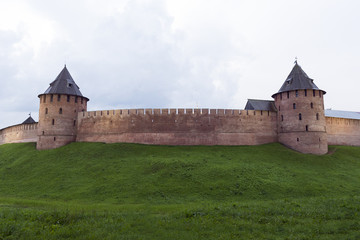 Obraz premium medieval fortification wall with towers of red brick, the Novgorod Kremlin, the green grass, rain clouds
