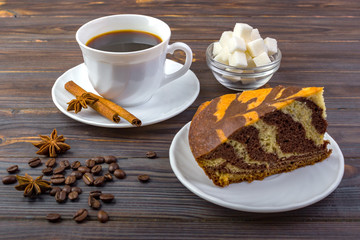 A cup of coffee with cinnamon sticks on a plate and a piece of tasty cake. Coffee beans. a bowl with sugar cubes and anise on wooden table