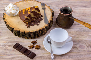 Obraz na płótnie Canvas Top view of a piece of chocolate cake on wooden stump with a coffee cup, tea spoon, fork, anise, coffee beans, chocolate bar and bowl with sugar cubes on a bright wooden background