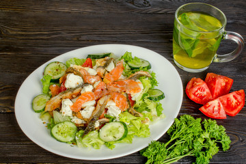 The concept of healthy diet. Salad of smoked salmon and smoked eel, with vegetables and lettuce leaves. And as well  glass mug with tea from mint and a bunch of parsley.