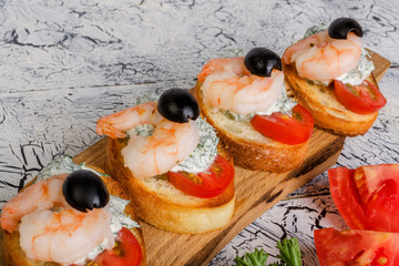 Delicious canapes with shrimps and sliced tomatoes on a wooden cutting board. And  parsley with tomato lies near.
