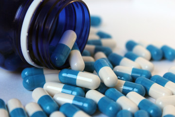 Blue and. tablets in a jar and around a jar of medicine