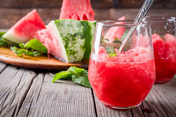 Summer fruit desserts, frozen cocktails. Ice cream granite from watermelon with mint, in portioned glasses, with slices of watermelon. On old rustic wooden table Copy space
