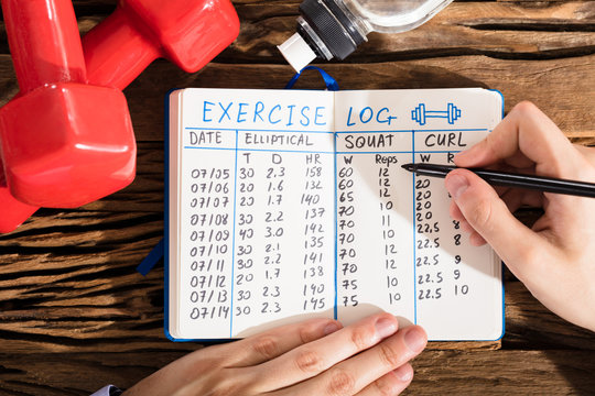 Elevated View Of A Hand Filling Exercise Log On Notebook