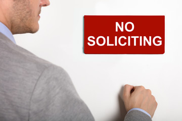 Businessman Knocking Door With No Soliciting Nameplate