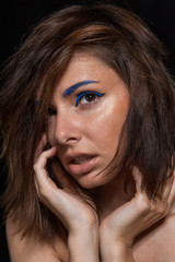 Unretouched portrait of a young pretty caucasian brunette girl posing in a studio on black background with soft light. She has messy hair and bright blue eye liner and beige lip gloss.