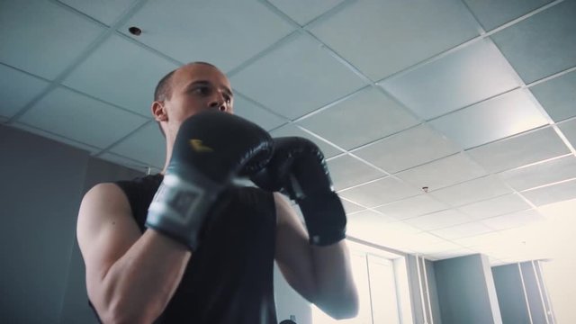 Sports and people, young male athlete training in boxing gym. Beats his fists at the camera. On the hands of boxing gloves.