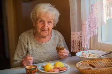 An elderly woman eats sitting at the table.