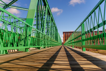Green metal bridge over river with nineteenth century brick mill buildings in background © Heidi Besen