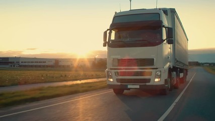 Front-View Camera Follows Semi-Truck with Cargo Trailer Driving on a Highway. He's Speeding Through Industrial Warehouse Area with Sunset in the Background. Shot on RED EPIC-W 8K Helium Cinema Camera. - Powered by Adobe