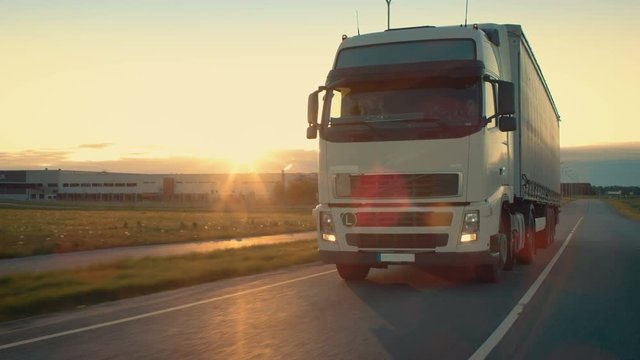 Front-View Camera Follows Semi-Truck with Cargo Trailer Driving on a Highway. He's Speeding Through Industrial Warehouse Area with Sunset in the Background. Shot on RED EPIC-W 8K Helium Cinema Camera.