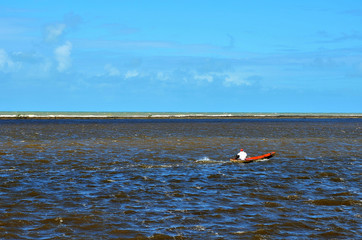 Small boat in the sea at river mouth protected by coral reefs in Porto Seguro, Bahia, Brazil. The sea in two colors separated by the coral barrier.