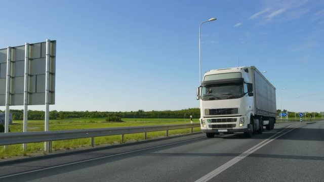 Big White Semi Truck with Cargo Trailer Drives on the Industrial Area Empty Road With Sun Shining in the Background. Shot on RED EPIC-W 8K Helium Cinema Camera.