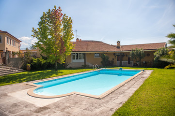 View on a luxury villa and a bright blue pool on a lawn. Shot on a hot summer sunny day with clear sky.