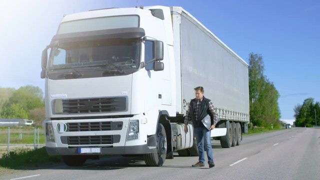 Truck Driver with Freight Documents Folder Gets out of His Parked White Cab-Over Truck and Crosses the Road. Shot on RED EPIC-W 8K Helium Cinema Camera.