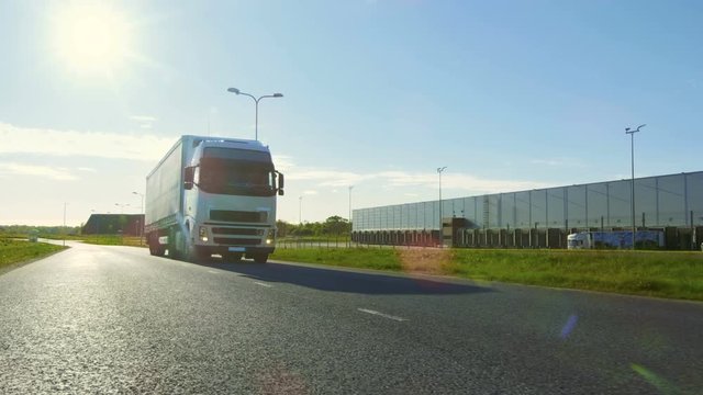 Big White Semi Truck with Cargo Trailer Moves on the Industrial Warehouse Area Empty Road With Sun Shining in the Background. Shot on RED EPIC-W 8K Helium Cinema Camera.