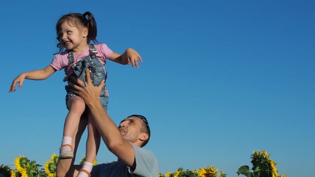 Father throws his daughter up. A happy father plays with a little daughter in sunflowers.