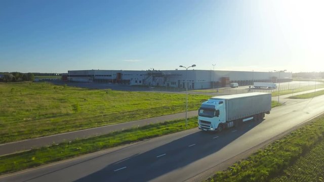 Aerial Follow Shot of White Truck with Semi Trailer Attached Moving Through Industrial Warehouse, Rural Area. Sunset. Shot on RED EPIC-W 8K Helium Cinema Camera.