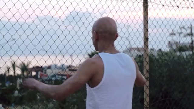 Angry bald man doing blows on fence grid. Angry bald man. Moor street