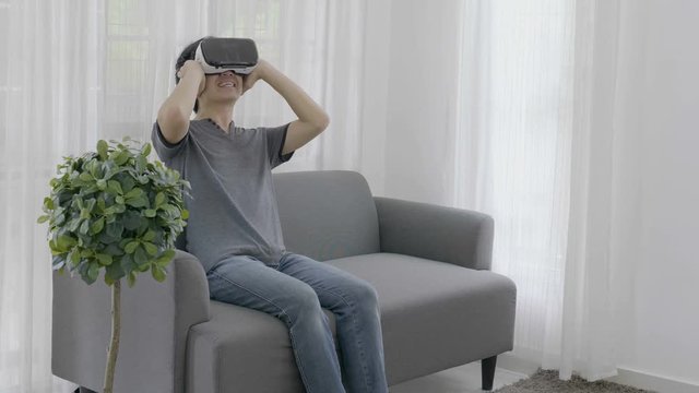 4K : Excited Asian young man wearing virtual reality goggles at home