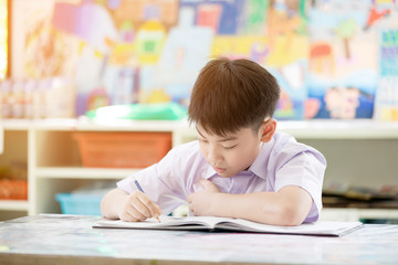 Portrait of happy asian cute child doing homework with smile face .