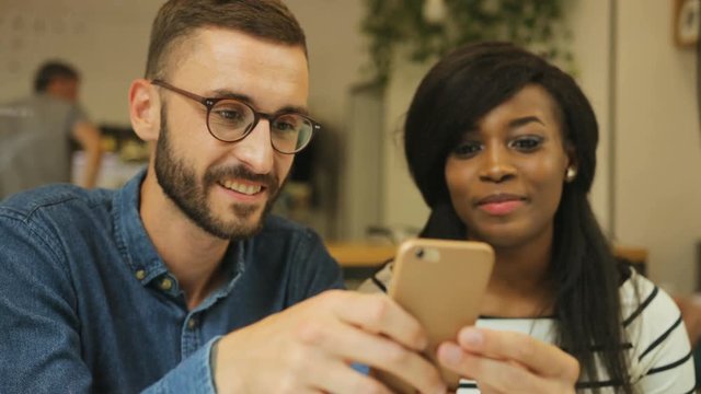 Close up shot of young attractive hipster drinking coffee with here female friend in the stylish cafe, man using smart phone while woman looking to the screen.