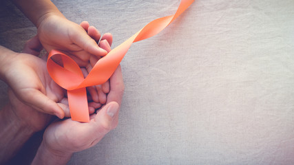 Adult and child hands holding orange Ribbons, Leukemia cancer awareness and Multiple sclerosis awareness, COPD,ADHD awareness, world kidney day - obrazy, fototapety, plakaty