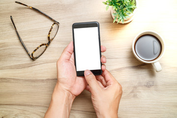 Hands of a man using blank smart phone. He is looking a mobile phone on the desk and the desk is make by the wood. Vintage effect style pictures.