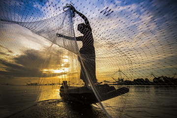 silhouette of fisherman with sunrise and big fish net in the background