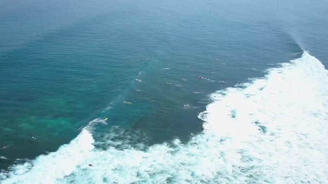 AERIAL: Beginners and pro surfers waiting in lineup to catch a breaking wave in crowded sunny Bali. Unrecognizable people on summer vacation swimming, paddling & surfing in crystal clear ocean