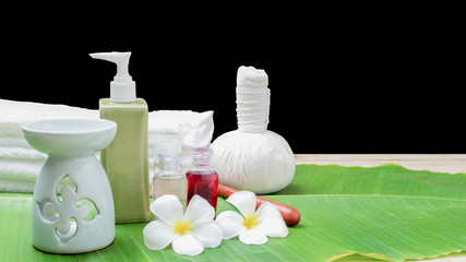 Spa massage equipment and plumeria flowers are placed on leaves on a black background with plenty of writing space.