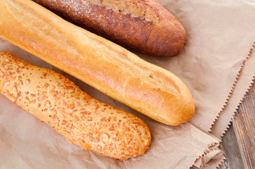Fresh crunchy baguette and cheese bun on paper bag and wooden table.