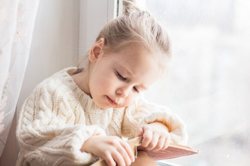 A little girl in the white knitted sweater with a book - 167429603
