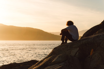 Man sitting on rocks near beach while sunset