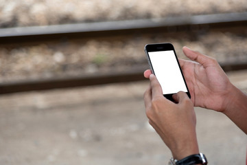 A man wearing a red shirt is using a cell phone while waiting for a train at the train station.