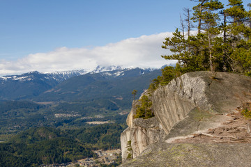 View point from cliff above valley with mountains and clouds.
