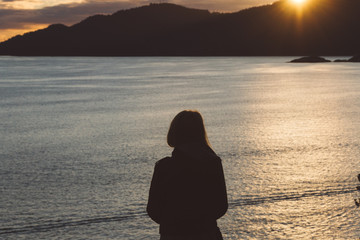 Fototapeta premium Silhouette of woman on coast with ocean and mountains while sunset