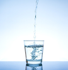 Pouring water and splashing in the glass with reflection on mirror.