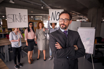 Unsatisfied employees on strike in the office, director standing with his back to employees. Modern office concept.