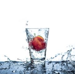 Red apple has droping to the glass and splashing water around the glass and on the table with reflection and isolated white background.