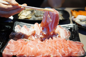 Hand holding raw pork using chopsticks for Japanese hot pot also known as Shabu Shabu or Sukiyaki...