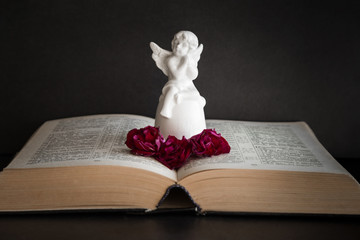 Little, white angel figurine on the opened bible. Quiet, dark atmosphere. Prayer time on sunday.