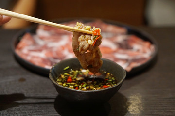 Hand holding raw pork using chopsticks with spicy sauce, Shabu Shabu or Sukiyaki is a Japanese style and Korean style.