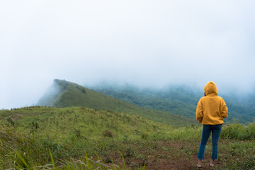 Naklejka premium Alone Girl with yellow overcoat and blue jeans has looking for way to the mountain in the heavy mist and cloudy.