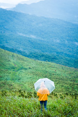 Fototapeta premium Alone female hiker holding umbrella and relaxing with big mountain and heavy mist under the cloudy sky.