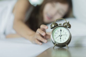 Selective focus  woman waking up and turning off the alarm clock. Not enough sleep concept.