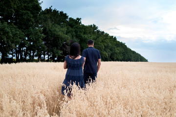 Naklejka na ściany i meble Happy young couple in love holding hands, walking and enjoying in oat field, summer season. Sunset light, copy space