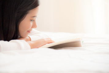 A young beautiful asian woman reading book on holiday. A closeup of a young happy girl lying on the cozy bed with opened book. Casual lifestyle at home.