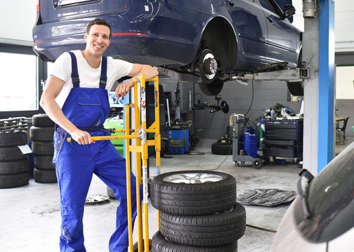 
    Reifenwechsel beim Auto - fröhlicher Mechaniker in einer Autowerkstatt - Dienstleistung wechsel der Bereifung am Fahrzeug 