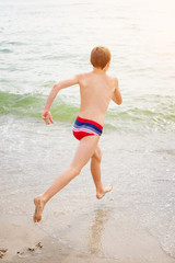 Boy running and jumping in sea waves. Summer vacation, sunny day, ocean coast. Toned image.